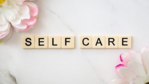 Self Care spelled out in scrabble pieces with pinkish flowers